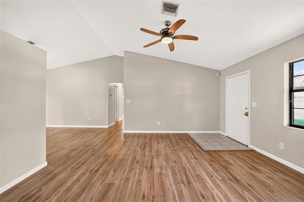An empty living room features wood-look flooring, a vaulted ceiling with a fan, and an entryway — 8 BANYAN COURSE RUN, OCALA, FL