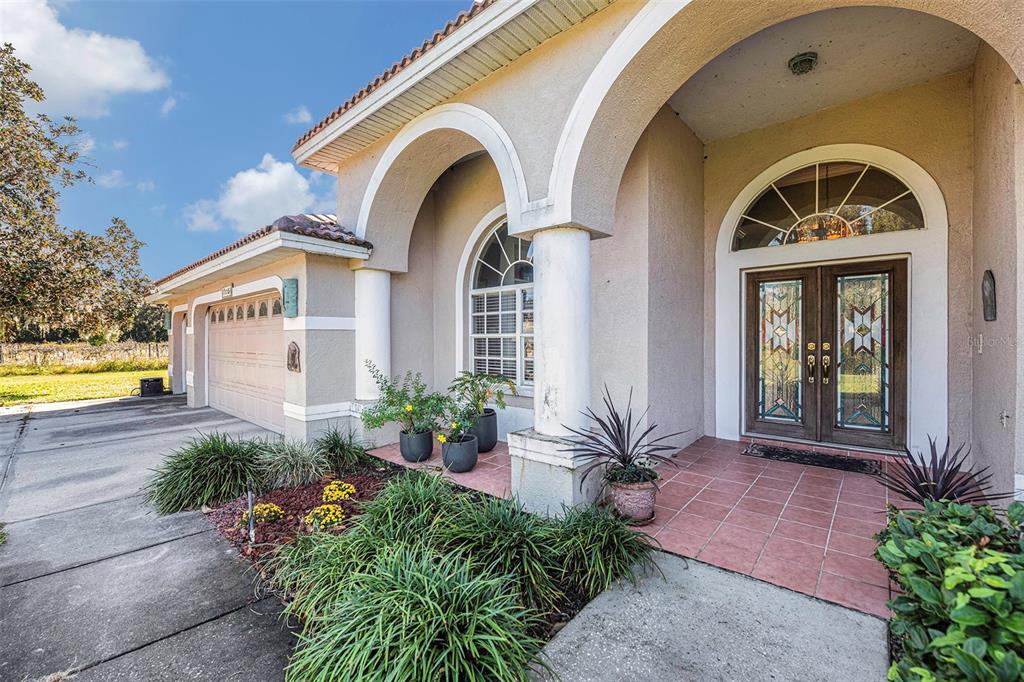 A tan stucco house exterior features a double front door, arched entryways, and a driveway — 331 LEWIS ROAD, LITHIA, FL