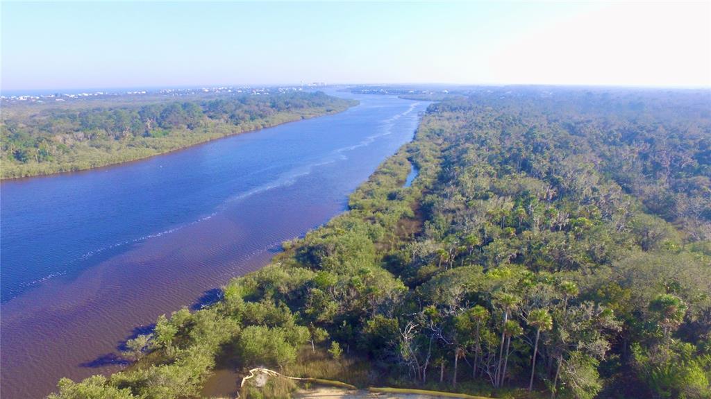An aerial view shows a wide river flowing through a dense, forested landscape — 140 CORONADO ROAD, FLAGLER BEACH, FL