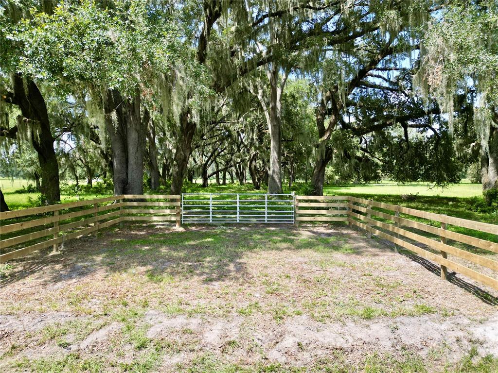 A metal gate stands between sections of a wooden fence in a grassy, tree-filled area — 00 C-478 W, WEBSTER, FL