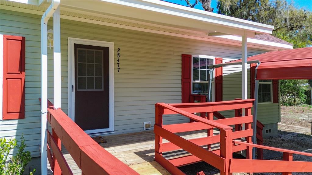 A light green house exterior features a wooden porch with red railings and a door — 28477 SENTINEL STREET, NOBLETON, FL