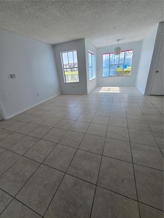 An empty room with light-colored tile flooring, white walls, and several windows overlooking water — 2214 GRAND CAYMAN COURT UNIT 1516, KISSIMMEE, FL