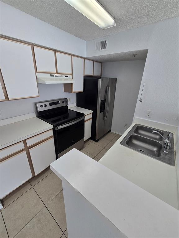 A kitchen features white cabinets, stainless steel appliances, a double sink, and tiled flooring — 2214 GRAND CAYMAN COURT UNIT 1516, KISSIMMEE, FL