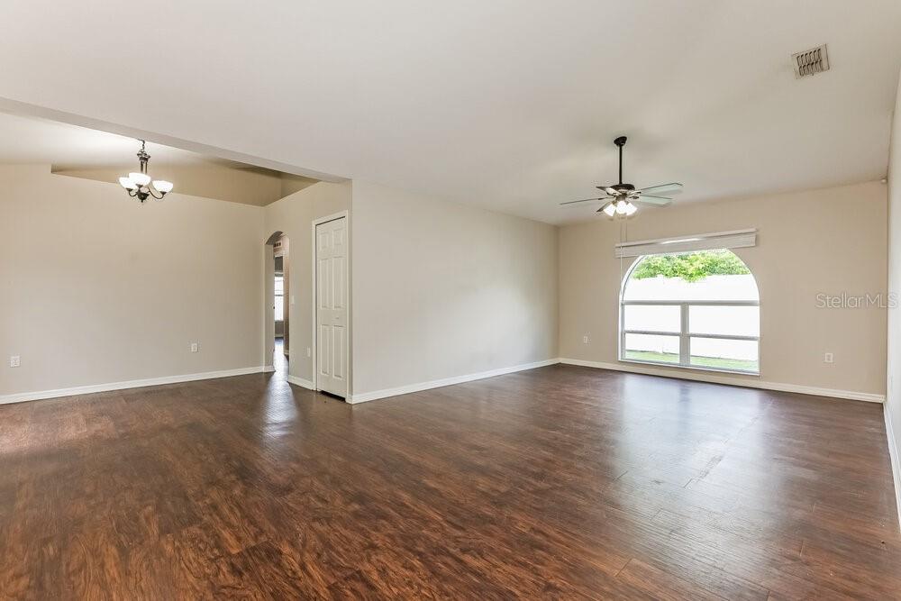An empty living room features dark wood-look flooring, a ceiling fan, and an arched window — 436 FISH HAWK DRIVE, WINTER HAVEN, FL