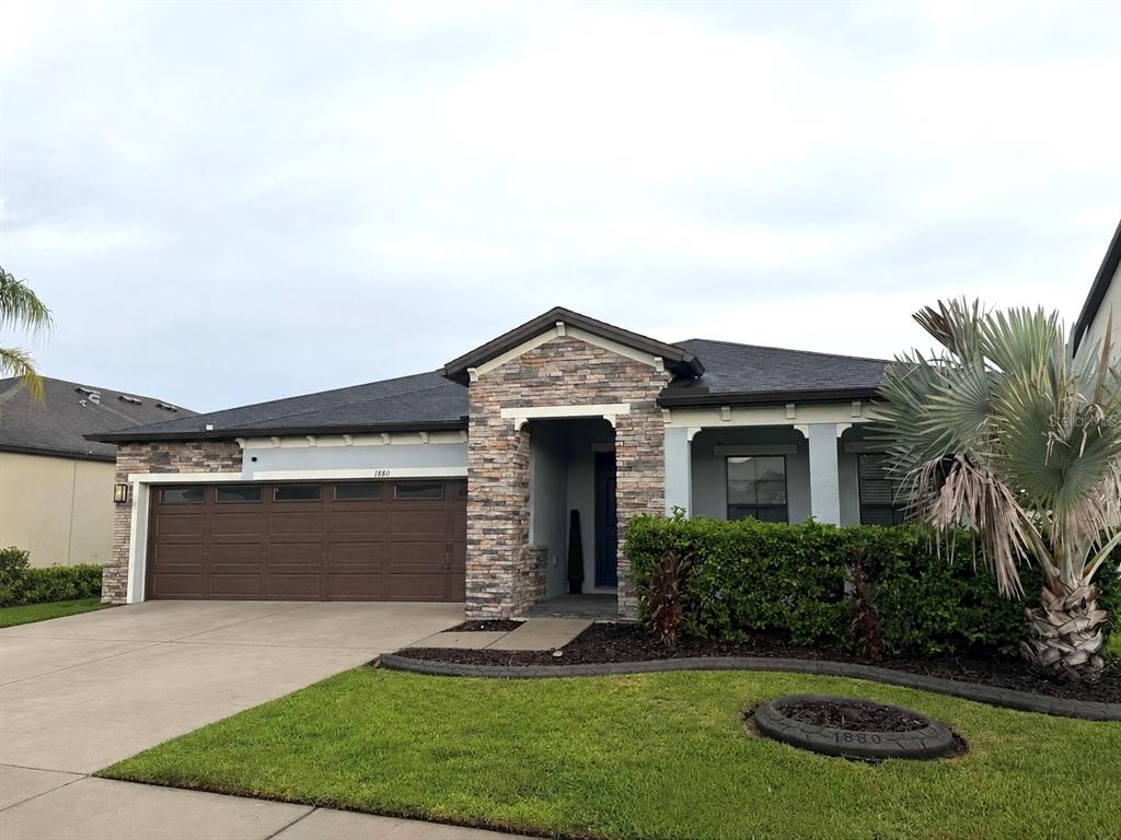 A single-story house features a stone-accented entryway, a brown garage door, and a landscaped lawn — 1880 TONKA TERRACE, WESLEY CHAPEL, FL