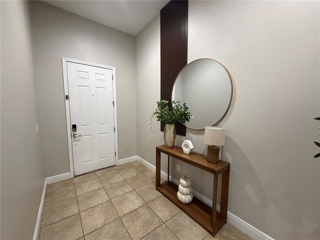 An entryway features a white door, tile flooring, a console table, and a round mirror — 1880 TONKA TERRACE, WESLEY CHAPEL, FL