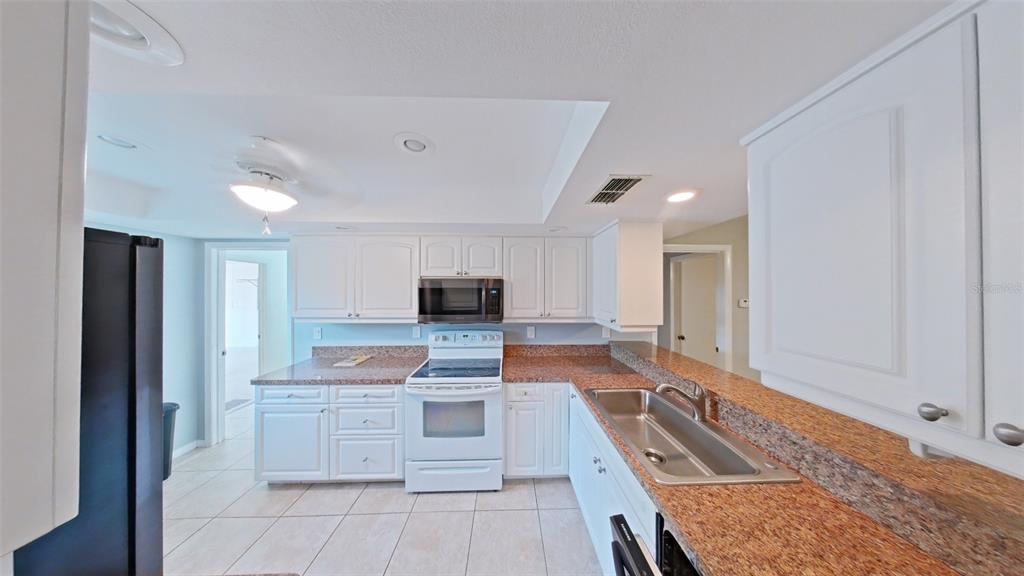 A kitchen features white cabinets, granite countertops, a stainless steel sink, and white appliances — 4602 LAFAYETTE AVENUE, SEBRING, FL