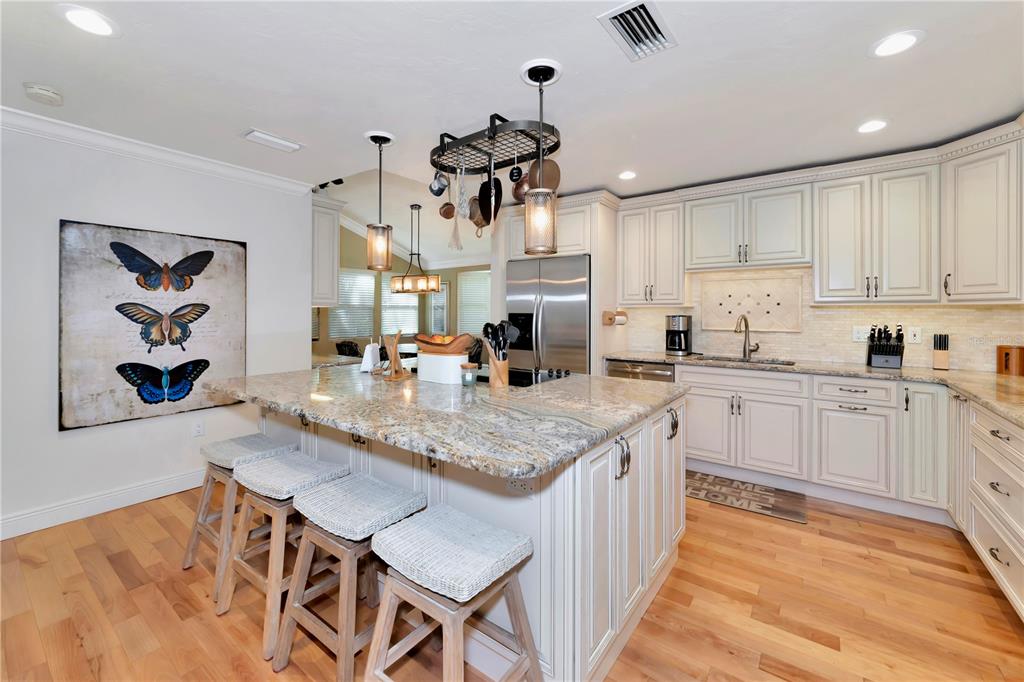 A kitchen with a granite-topped island, light-colored cabinetry, and a butterfly wall art piece — 4737 STONE RIDGE TRAIL, SARASOTA, FL