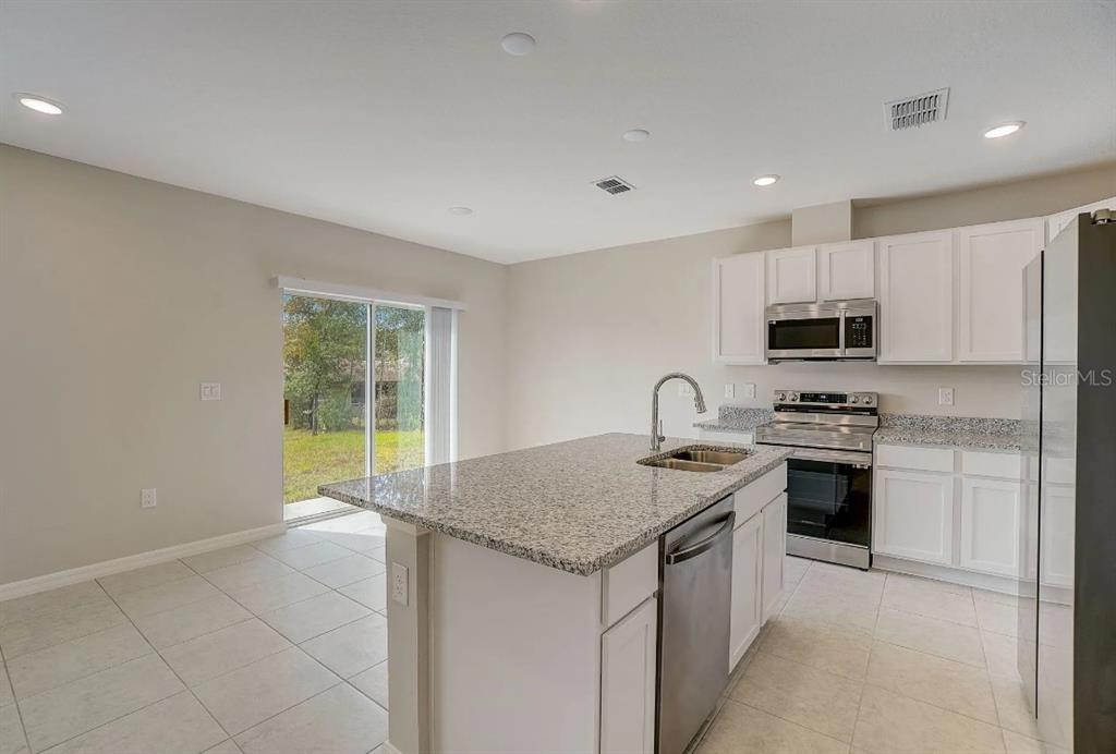 A kitchen with white cabinets, granite countertops, a center island, and a sliding glass door — 16849 NW 176TH WAY, ALACHUA, FL