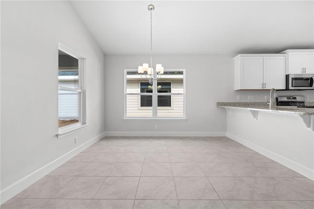 A dining area with tile floors, a chandelier, and an adjacent kitchen with white cabinets — 39 RIVERINA DRIVE, PALM COAST, FL