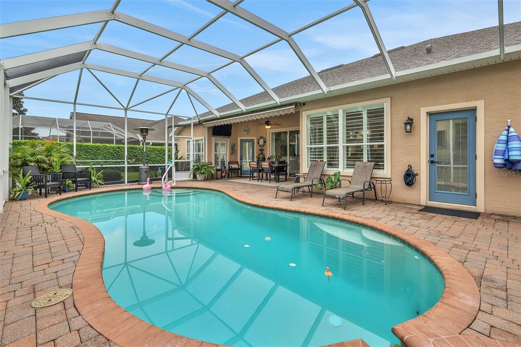 A screened-in patio features a kidney-shaped swimming pool, brick pavers, and outdoor seating — 1244 HARWICK LANE, ORMOND BEACH, FL