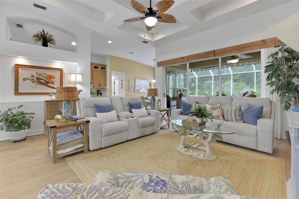 A bright living room features a tray ceiling, light wood floors, and neutral furniture — 1244 HARWICK LANE, ORMOND BEACH, FL