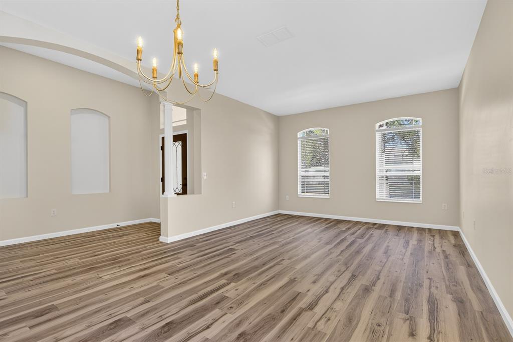 An empty room with wood-look flooring, a gold chandelier, and two arched wall niches — 6002 MARTINGLADE PLACE, LITHIA, FL