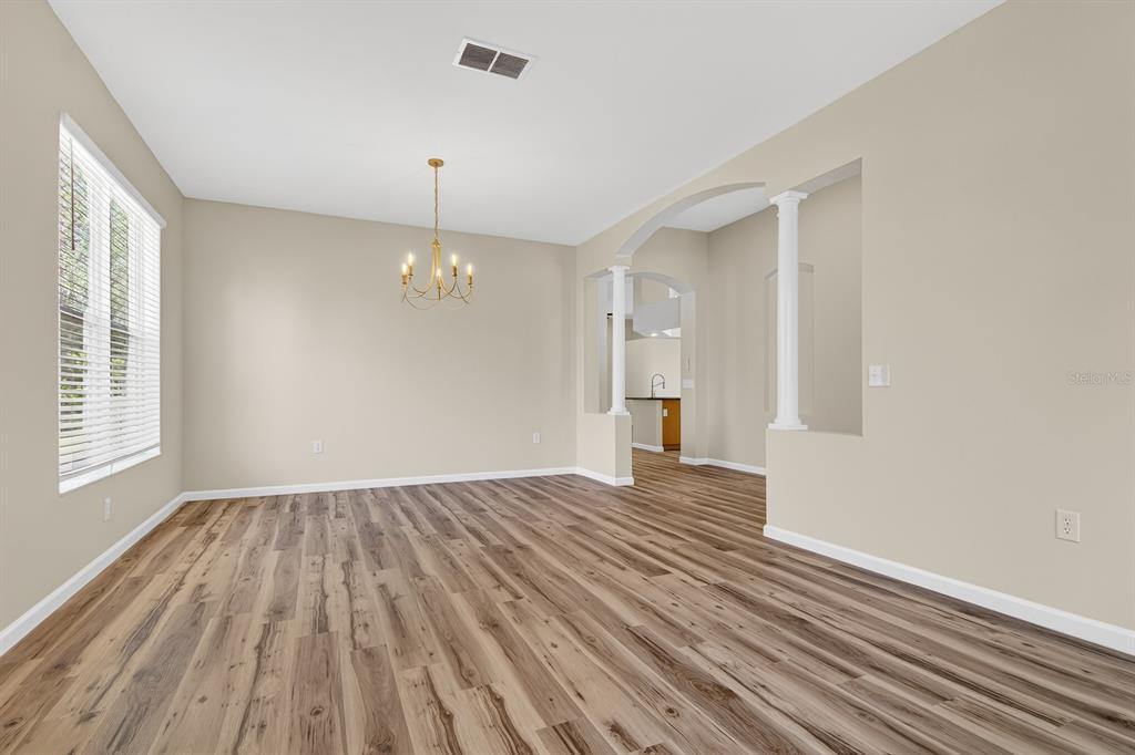 A dining room with wood-look flooring, a chandelier, and an arched entryway to the kitchen — 6002 MARTINGLADE PLACE, LITHIA, FL