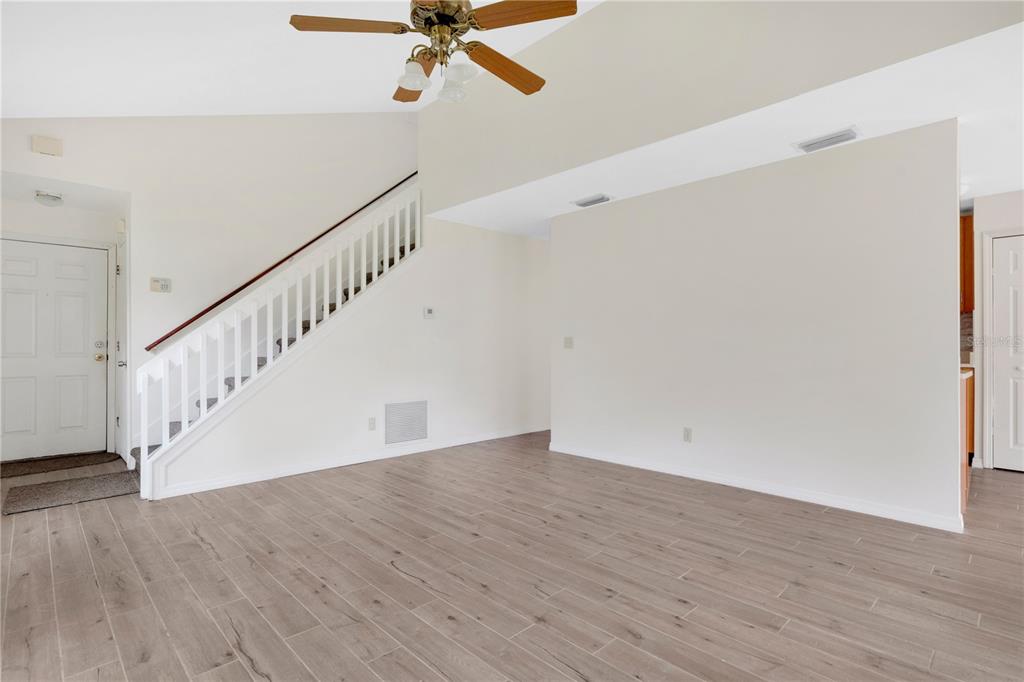 A living room features light wood-look flooring, white walls, a ceiling fan, and a staircase — 11842 ATLIN DRIVE, ORLANDO, FL
