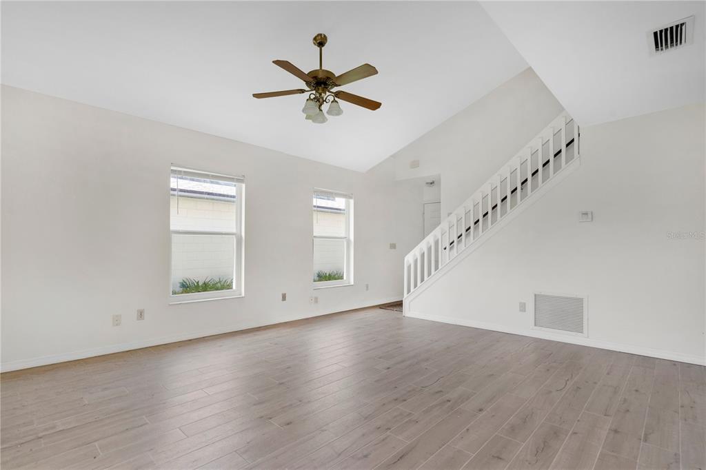 An empty room with light wood-look tile flooring, a vaulted ceiling, and sliding glass doors — 11842 ATLIN DRIVE, ORLANDO, FL