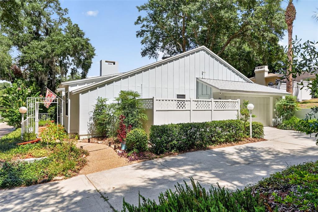 A white house with vertical siding, a garage, and a privacy fence sits near trees — 21 TOWNHILL DRIVE, EUSTIS, FL