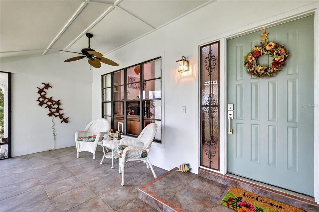 A covered porch features tiled flooring, two white wicker chairs, and a light blue front door — 21 TOWNHILL DRIVE, EUSTIS, FL