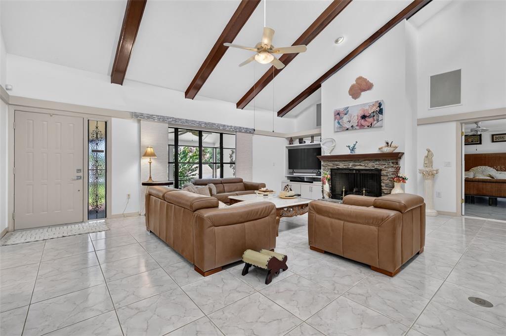 A living room features vaulted ceilings with exposed beams, a stone fireplace, and tile flooring — 21 TOWNHILL DRIVE, EUSTIS, FL