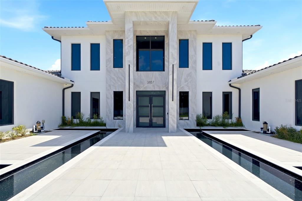 A modern two-story house features a marble-clad entrance with a central doorway and reflecting pools — 3857 S STILLWOOD LANE, LAKE MARY, FL