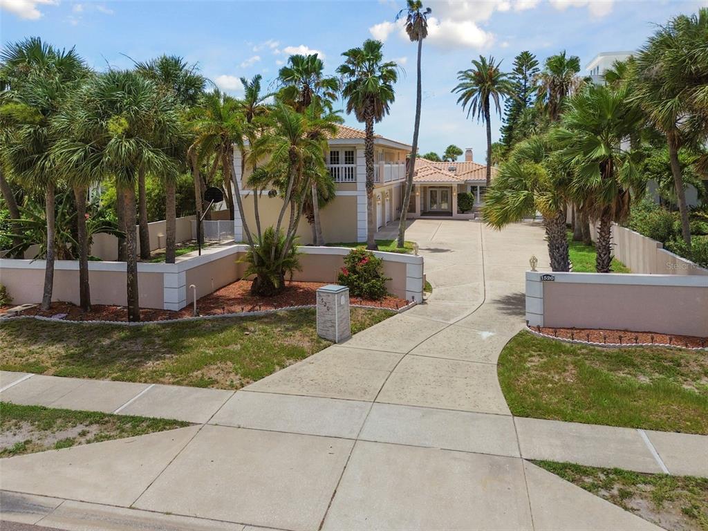 An exterior view of a two-story house with a large concrete driveway and palm trees — 1520 GULF BOULEVARD, BELLEAIR BEACH, FL