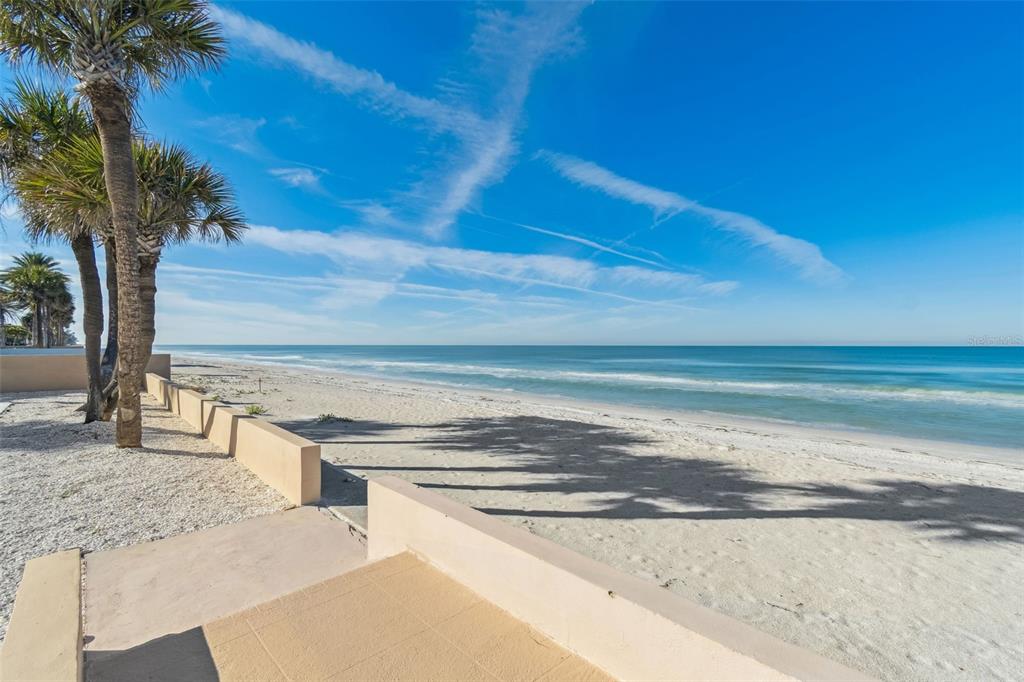 A view of a sandy beach and ocean from a paved patio with palm trees — 1520 GULF BOULEVARD, BELLEAIR BEACH, FL