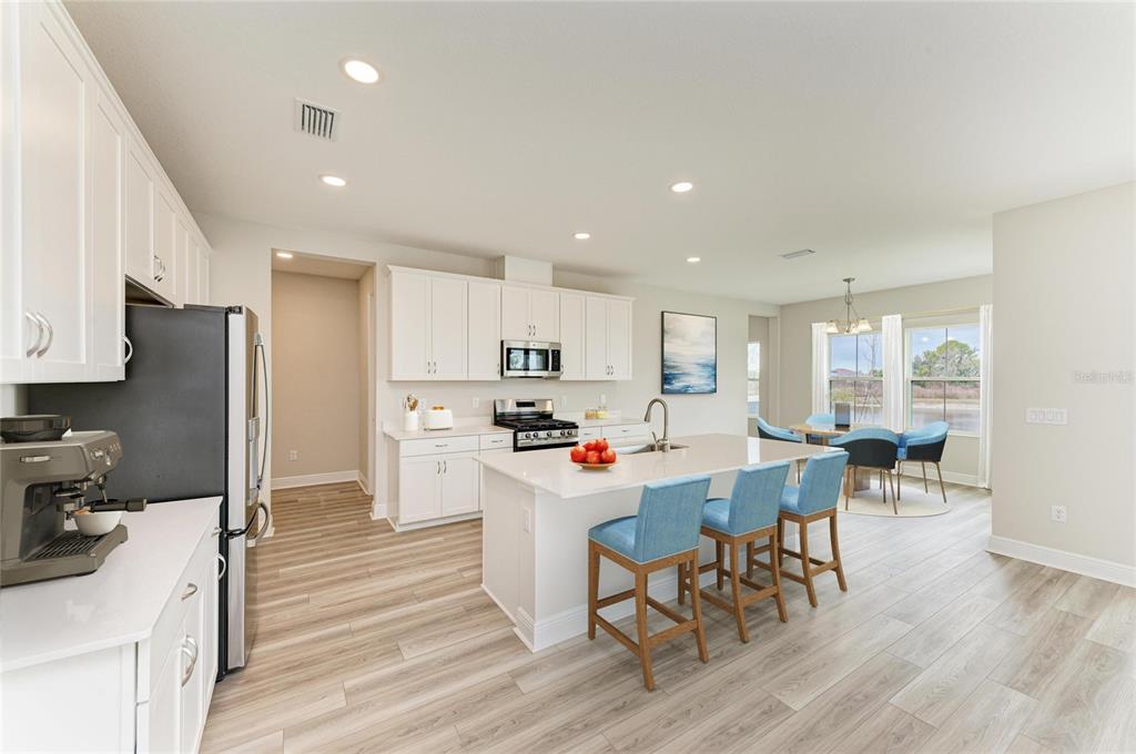 A modern kitchen features white cabinets, a central island with blue stools, and wood flooring — 13718 HEARTWOOD WAY, PARRISH, FL