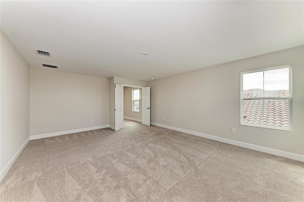 A spacious, carpeted bedroom features beige walls, a window, and double doors leading to another room — 13718 HEARTWOOD WAY, PARRISH, FL