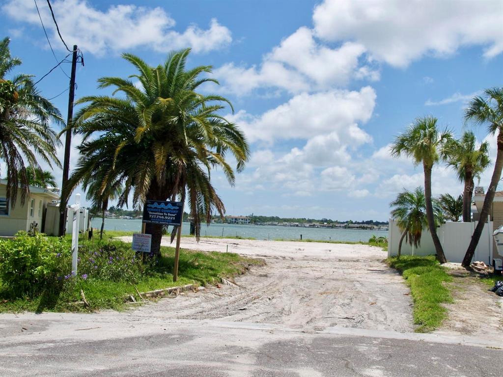 A vacant waterfront lot features palm trees, a dirt driveway, and a demolition company sign — 16003 5TH STREET E, REDINGTON BEACH, FL