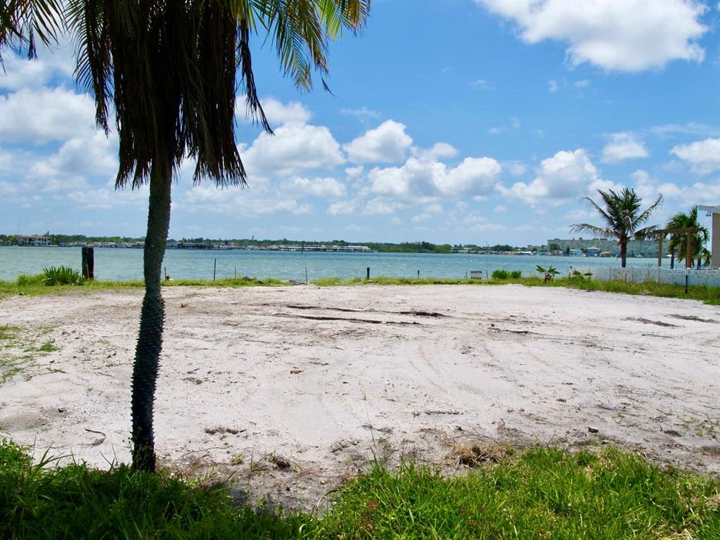 A sandy, cleared waterfront lot features a palm tree in the foreground under a blue sky — 16003 5TH STREET E, REDINGTON BEACH, FL