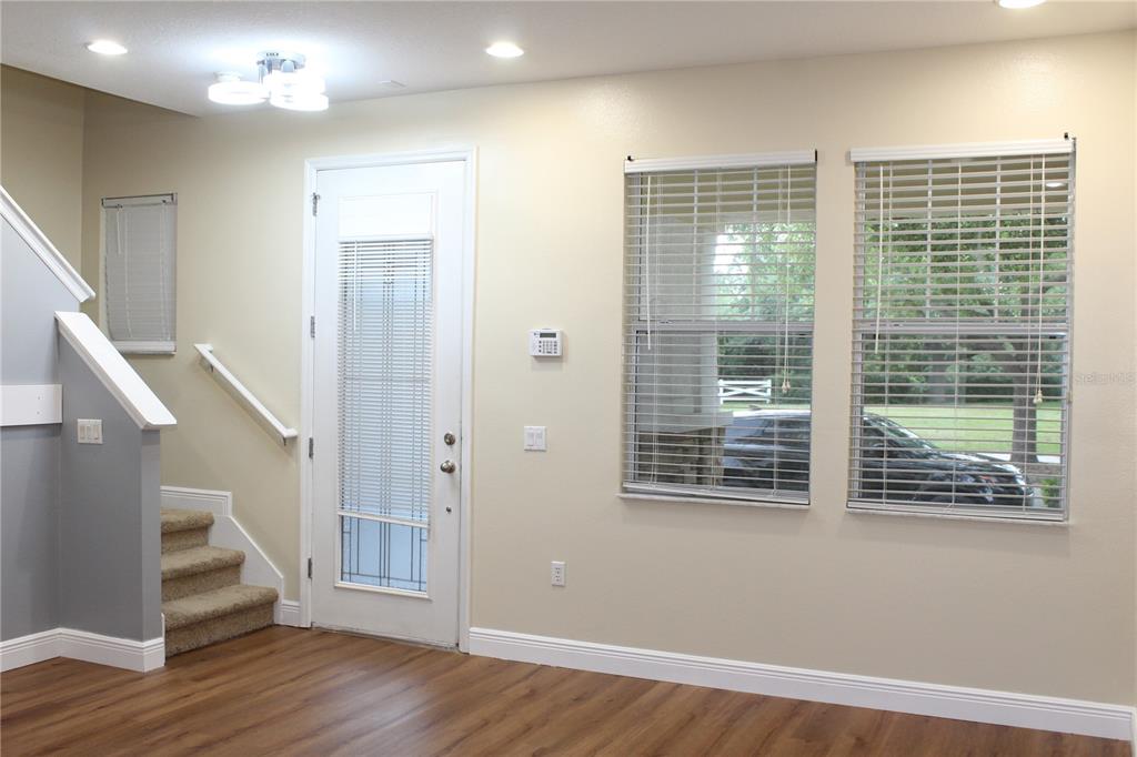 A living room with wood-look flooring, a staircase, a glass-paneled door, and two windows — 7365 BRIGHTLAND STREET, WINDERMERE, FL