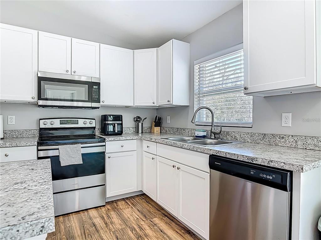 A kitchen features white cabinets, granite countertops, stainless steel appliances, and wood-look flooring — 640 CHESTNUT AVENUE, ORANGE CITY, FL