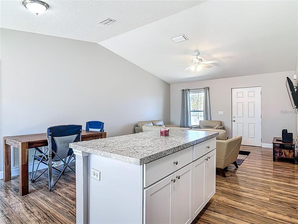 A kitchen island with granite countertops sits in an open-concept living area with wood flooring — 640 CHESTNUT AVENUE, ORANGE CITY, FL