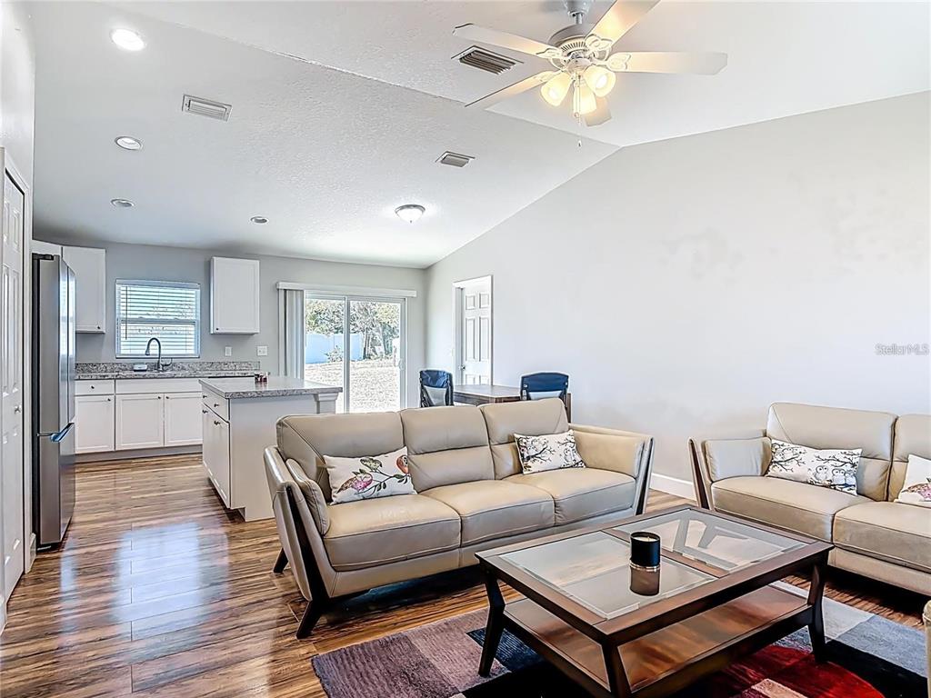 An open-concept living room and kitchen featuring light-colored sofas, wood-look flooring, and a ceiling fan — 640 CHESTNUT AVENUE, ORANGE CITY, FL