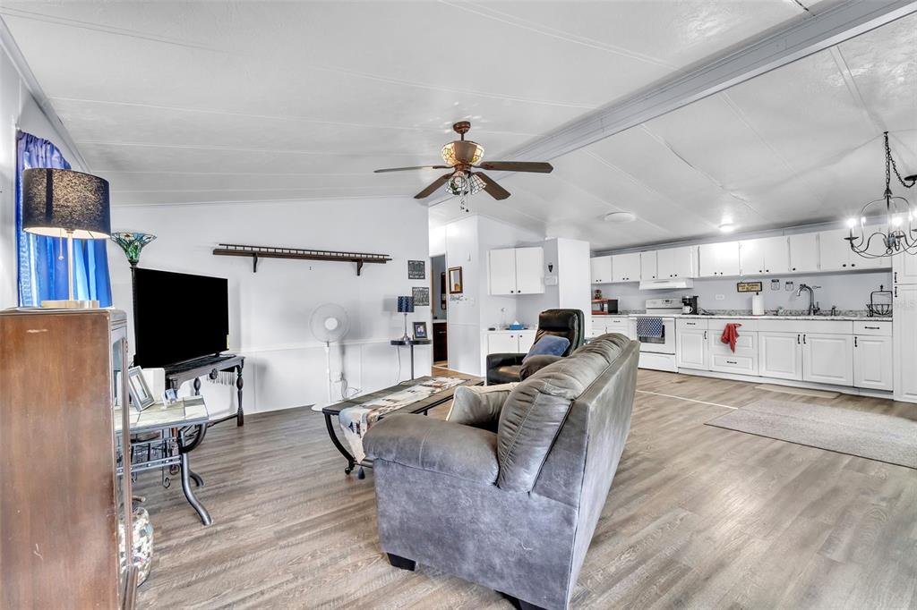 An open-concept living room and kitchen featuring white cabinetry, wood-look flooring, and a ceiling fan — 2576 LAKOTA LANE, ST CLOUD, FL