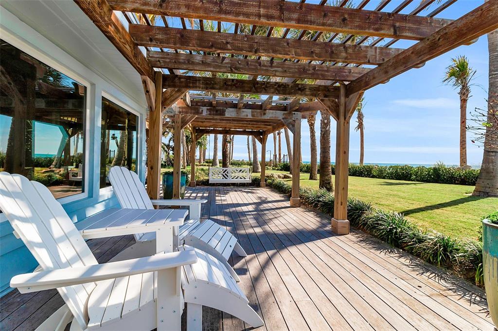 A wooden pergola covers a deck with white Adirondack chairs overlooking a grassy lawn — 621 CASEY KEY ROAD, NOKOMIS, FL