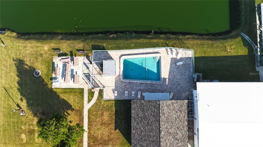 An aerial view shows a backyard with a swimming pool, patio, and adjacent pond — 306 50TH AVENUE PLAZA E, BRADENTON, FL