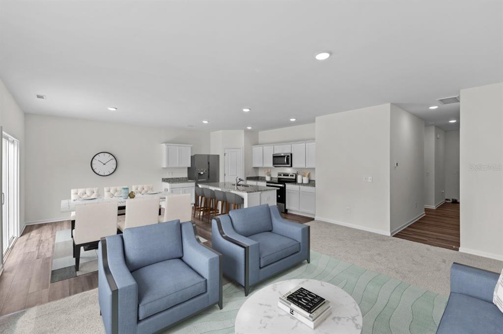 An open-concept living and dining area features blue armchairs, a kitchen island, and white cabinetry — 10539 CURVING CREEK LOOP, PARRISH, FL