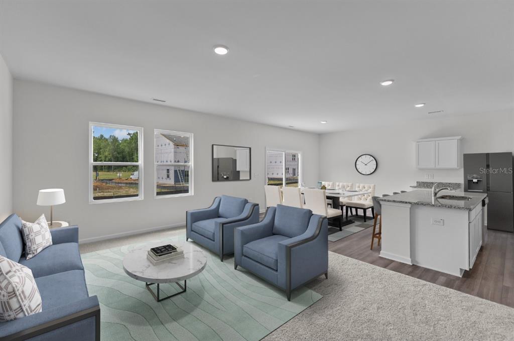 This open-concept living and dining area features blue furniture, a kitchen island, and neutral finishes — 10539 CURVING CREEK LOOP, PARRISH, FL