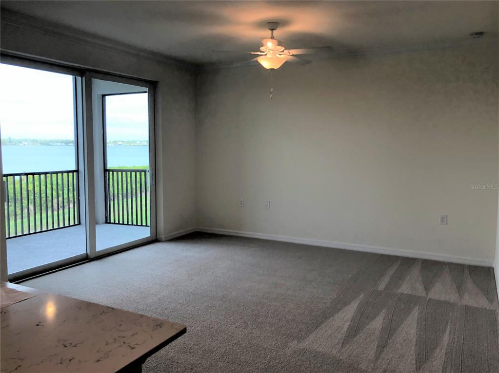 A carpeted living room features a ceiling fan and sliding glass doors opening to a balcony — 1010 TIDEWATER SHORES LOOP UNIT 206, BRADENTON, FL