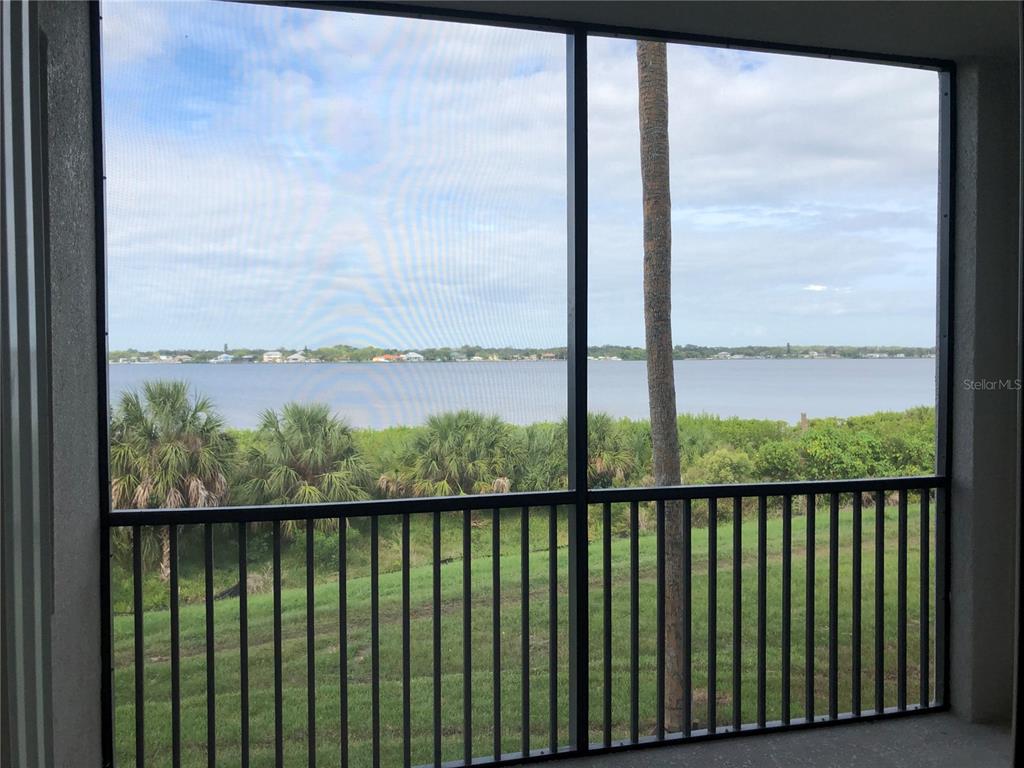 A screened-in porch overlooks a grassy yard, lush vegetation, and a large body of water — 1010 TIDEWATER SHORES LOOP UNIT 206, BRADENTON, FL