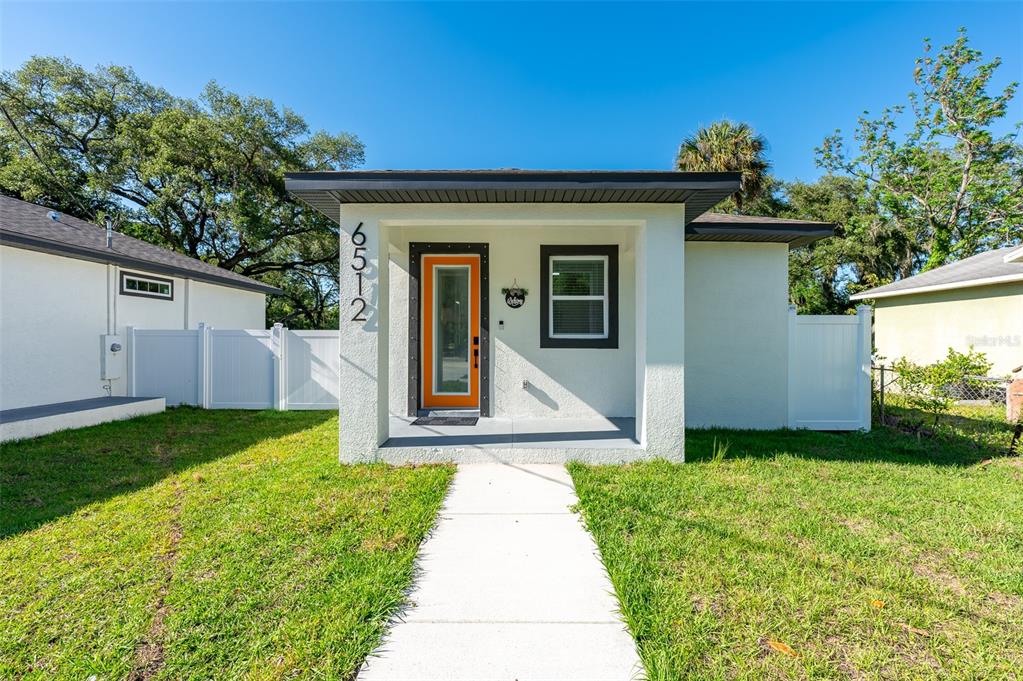 A single-story house with a white exterior, a bright orange front door, and a walkway — 6510 E 25TH AVENUE, TAMPA, FL