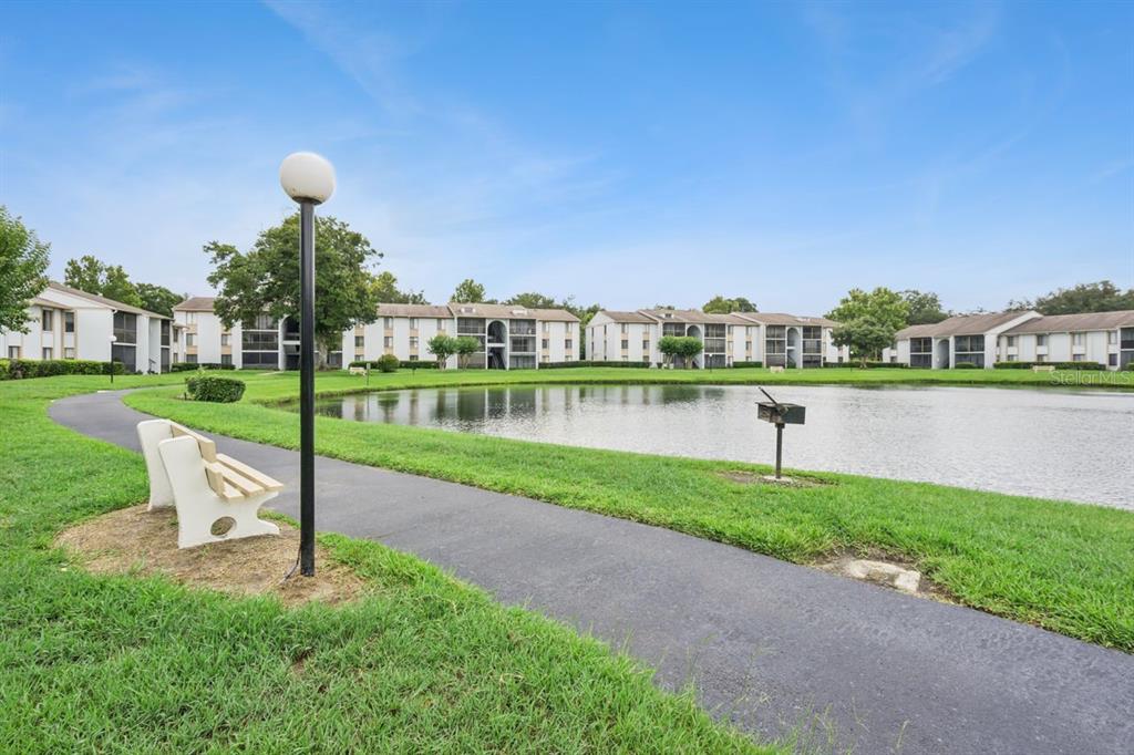 A paved path curves around a pond in front of multi-story apartment buildings — 8215 SUN SPRING CIRCLE UNIT 12, ORLANDO, FL
