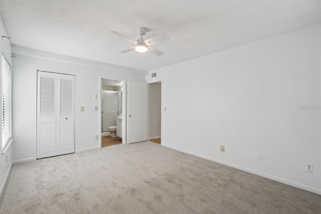 A bedroom with white walls, gray carpet, a ceiling fan, and an attached bathroom — 8215 SUN SPRING CIRCLE UNIT 12, ORLANDO, FL