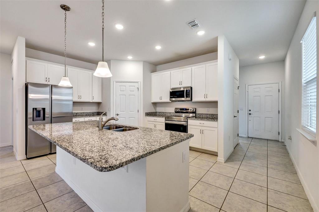 A kitchen with white cabinets, granite countertops, a center island, and stainless steel appliances — 2599 AVALON PARK BOULEVARD, TAVARES, FL