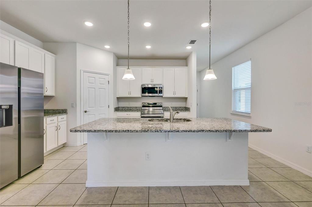 A kitchen features white cabinets, granite countertops, a central island, and stainless steel appliances — 2599 AVALON PARK BOULEVARD, TAVARES, FL