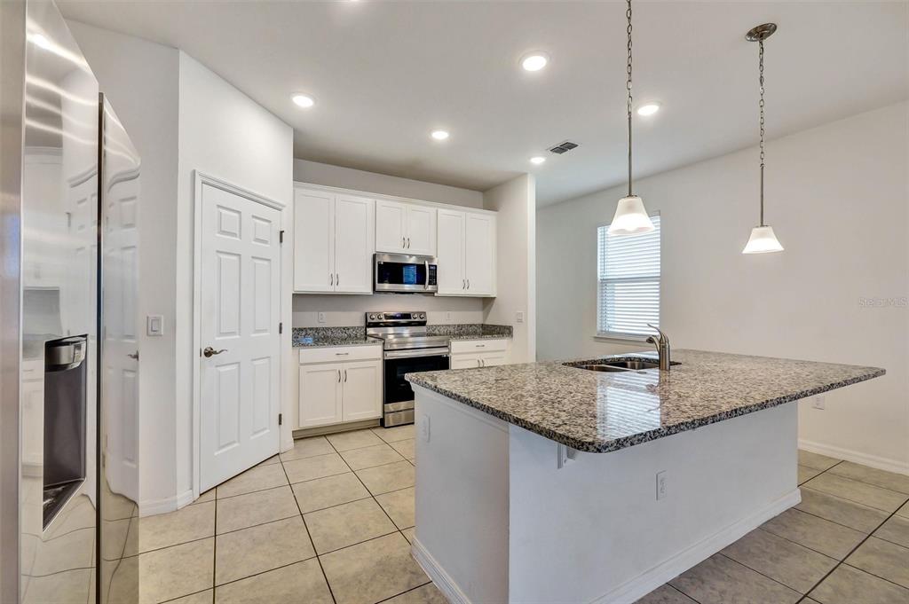 A kitchen features white cabinets, granite countertops, a center island, and stainless steel appliances — 2599 AVALON PARK BOULEVARD, TAVARES, FL