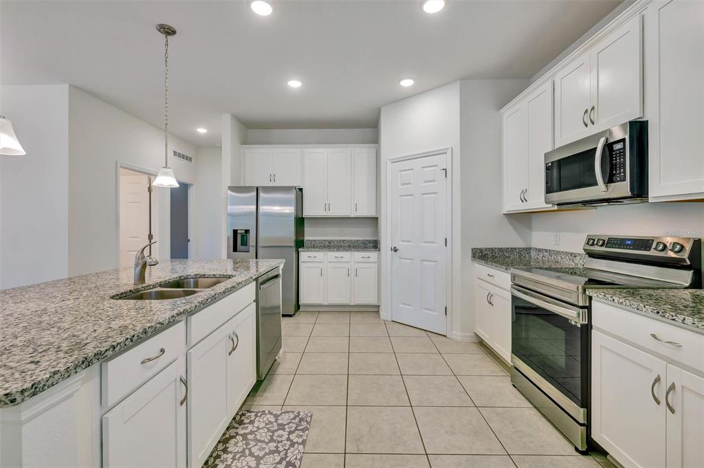 A kitchen with white cabinets, granite countertops, stainless steel appliances, and light tile flooring — 2599 AVALON PARK BOULEVARD, TAVARES, FL