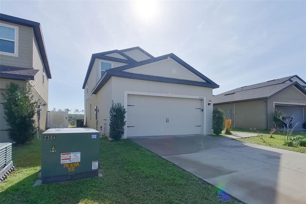 A single-family home exterior features a two-car garage, a concrete driveway, and a utility transformer — 30098 FEDORA CIRCLE, BROOKSVILLE, FL