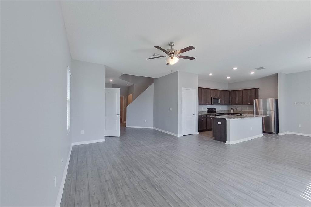 An open-concept living room features gray wood-look flooring, a ceiling fan, and a kitchen area — 30098 FEDORA CIRCLE, BROOKSVILLE, FL